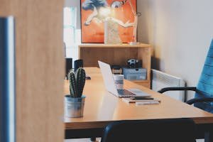 A modern office desk setup featuring a cactus plant, laptop, and stylish decor in a contemporary office space.