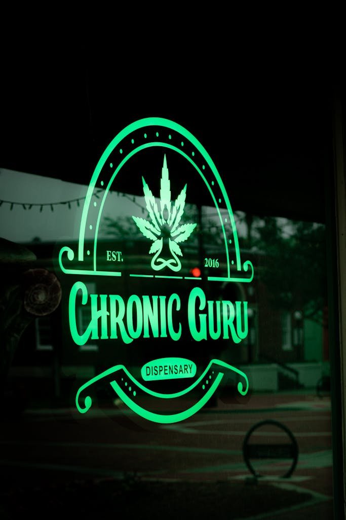 Neon sign of Chronic Guru Dispensary with cannabis leaf, glowing against dark urban background.