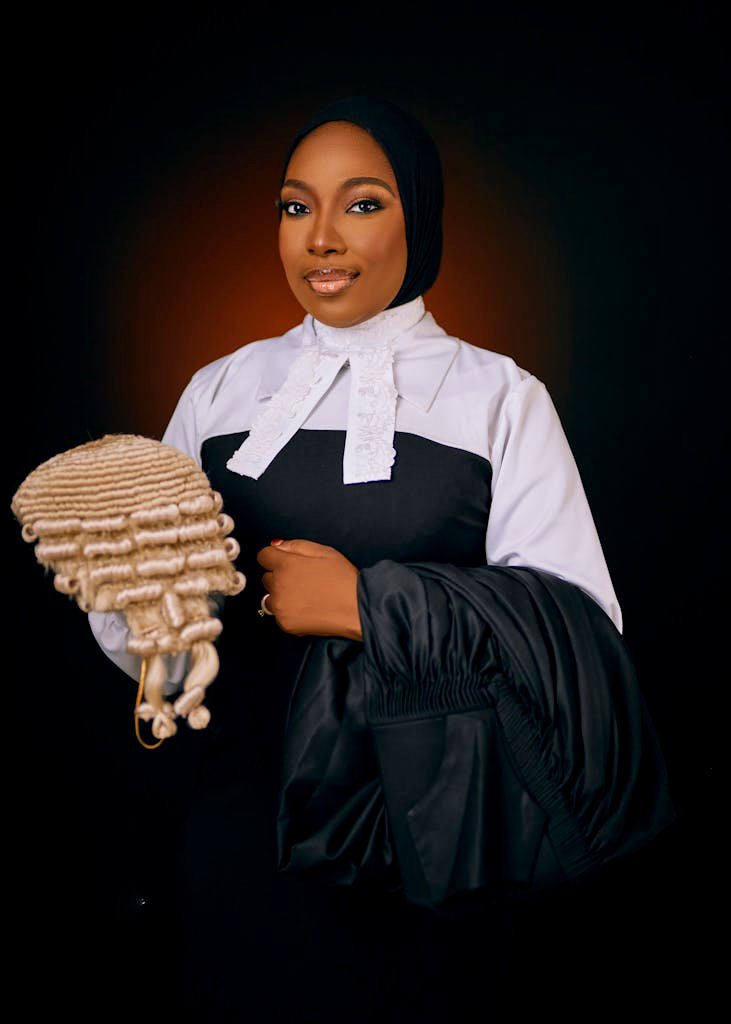 Portrait of a poised female lawyer in courtroom attire holding a barrister wig against a dark backdrop.