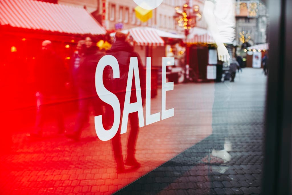 Red sale sign on storefront window reflecting a busy urban street scene, capturing city life.